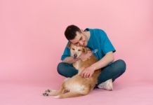 A person hugging a dog. They are sitting down against a pink background.