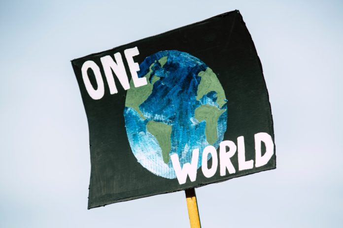 A climate change protest sign. The sign is black, with a painting of the Earth in the middle. The words 