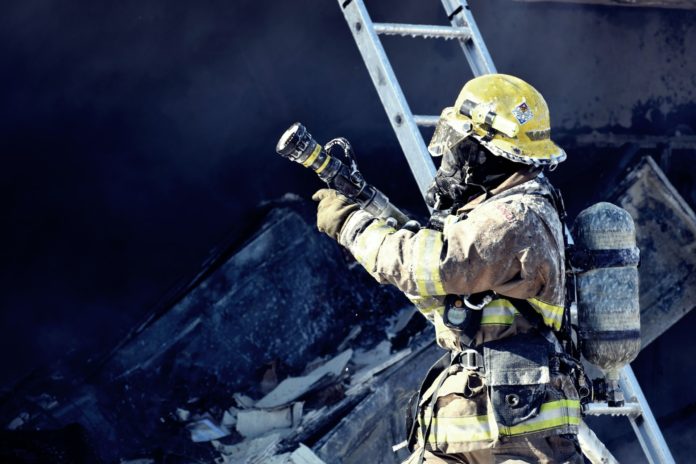 A firefighter standing on a ladder while holding a hose.