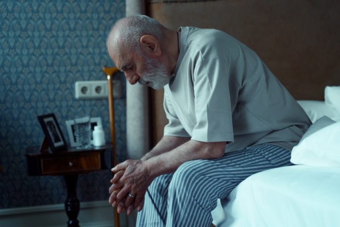 A sad elderly person sitting alone in bed.