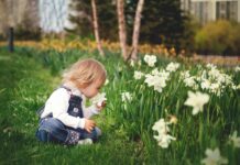 A child sitting in a park and smelling a flower.